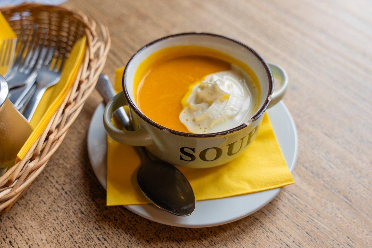 Ambiance cozy winter soup setting avec une soupe de potiron crémeuse dans un mug en émail rustique.