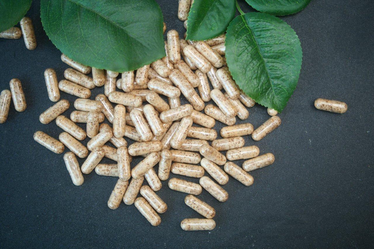 Capsules de ginseng rouge bio organique posées sur des feuilles vertes, idéales pour la santé et le bien-être naturel.