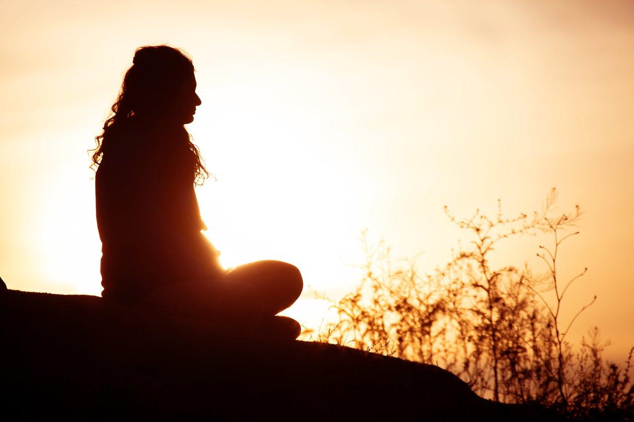 Person meditating calm light, favorisant la sérénité et la relaxation face à un coucher de soleil apaisant.