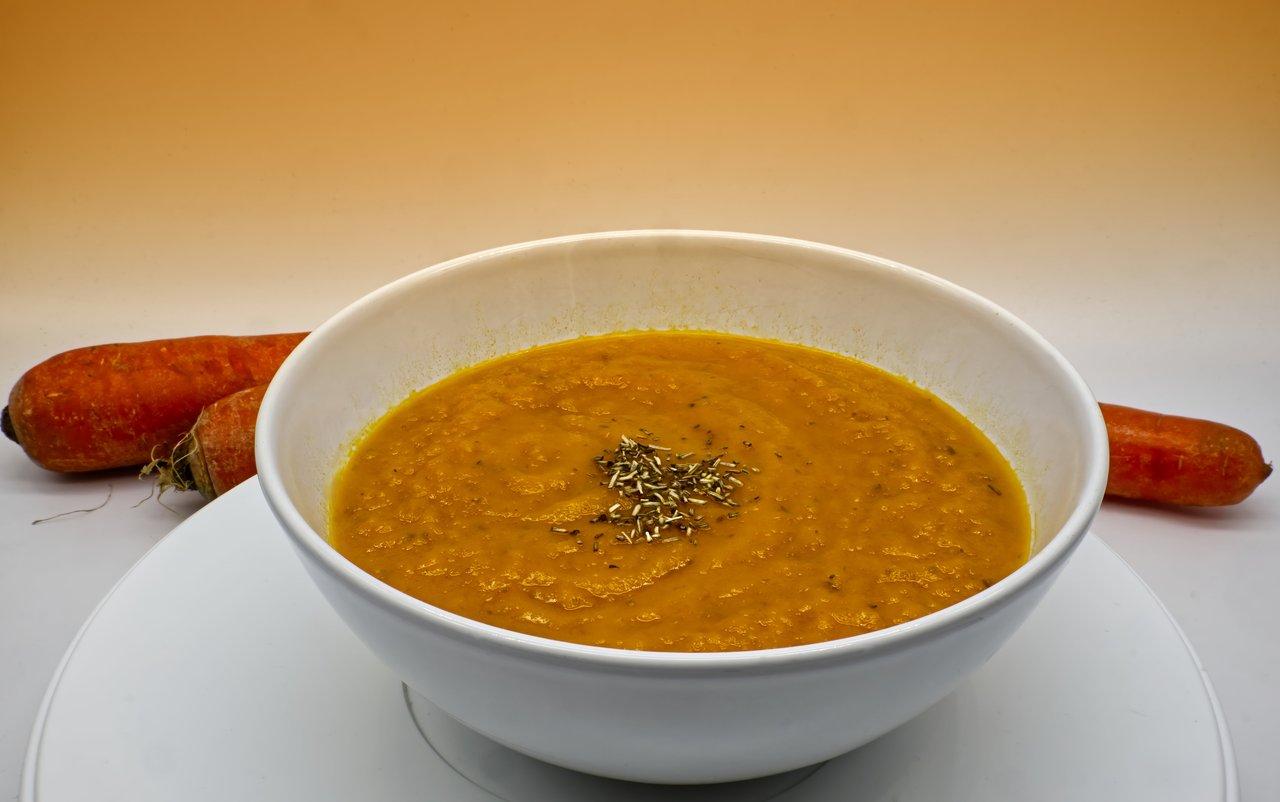 Soupe de légumes racines d’hiver, riche et crémeuse, garnie d’herbes fraîches dans un bol blanc.
