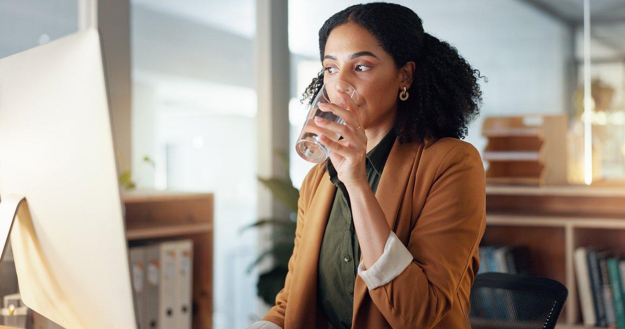 Une femme au bureau pratique une hydratation saine avec un verre d’eau aromatisée et une salade fraîche.